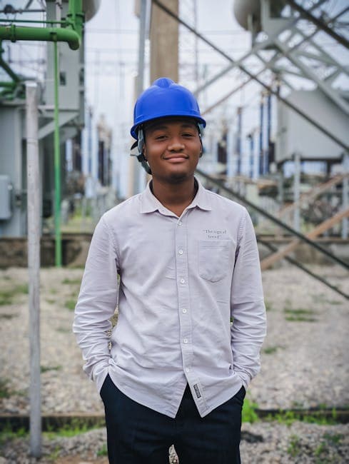 A young engineer wearing a hard hat stands at an electrical substation in Kaduna, Nigeria.
