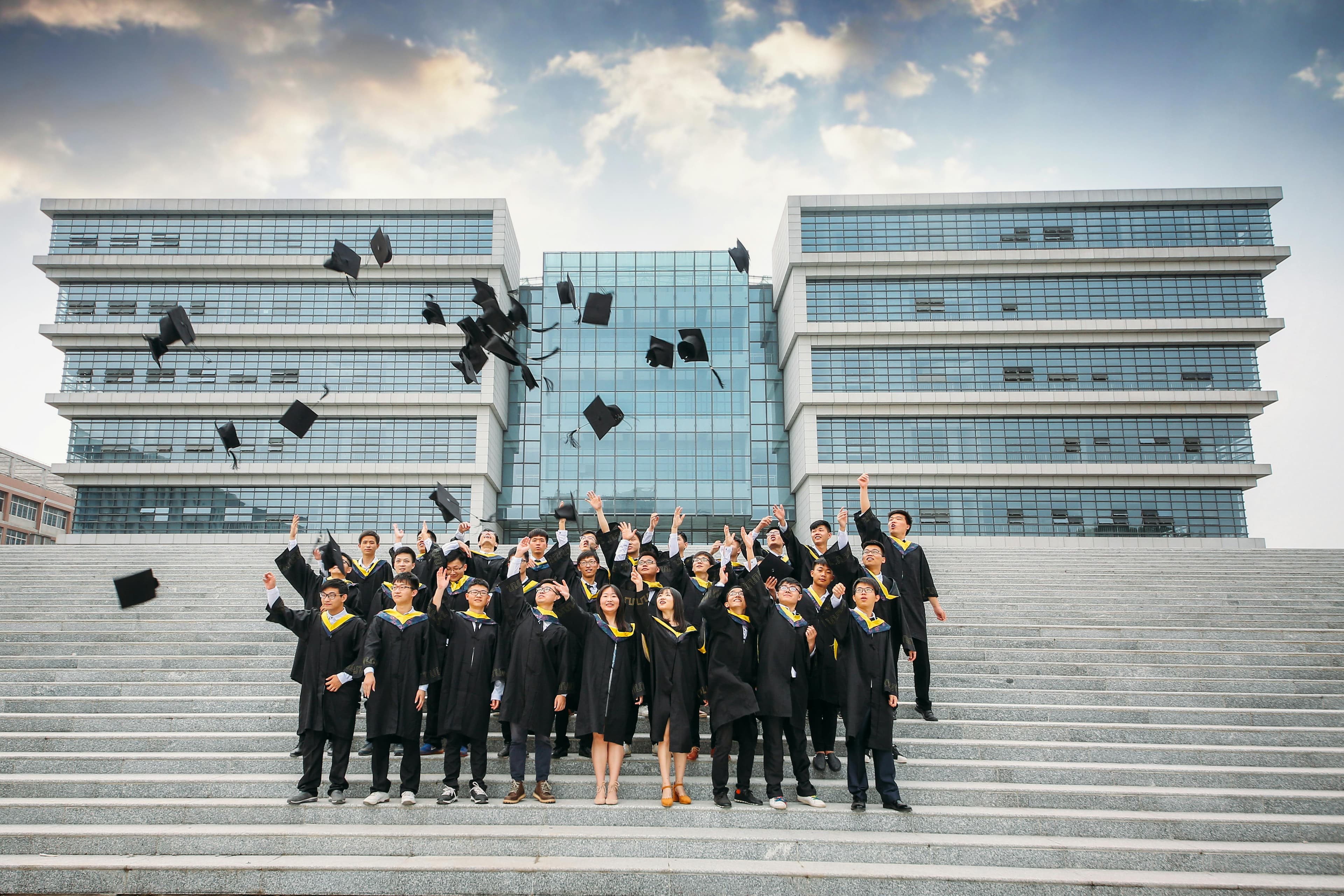 Group of graduates celebrating and tossing caps outside modern building.