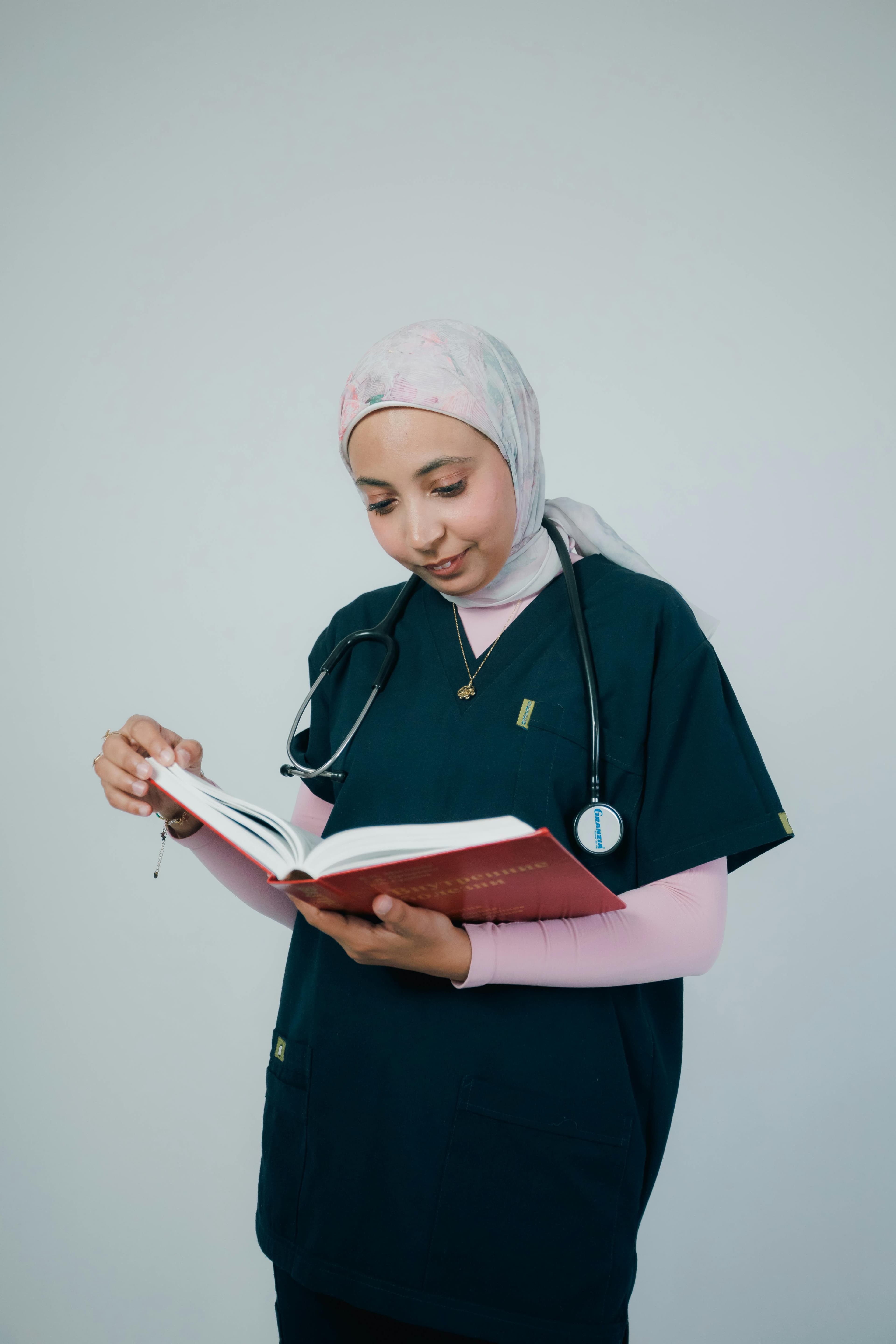 Medical professional in scrubs reading a book with focus and concentration.