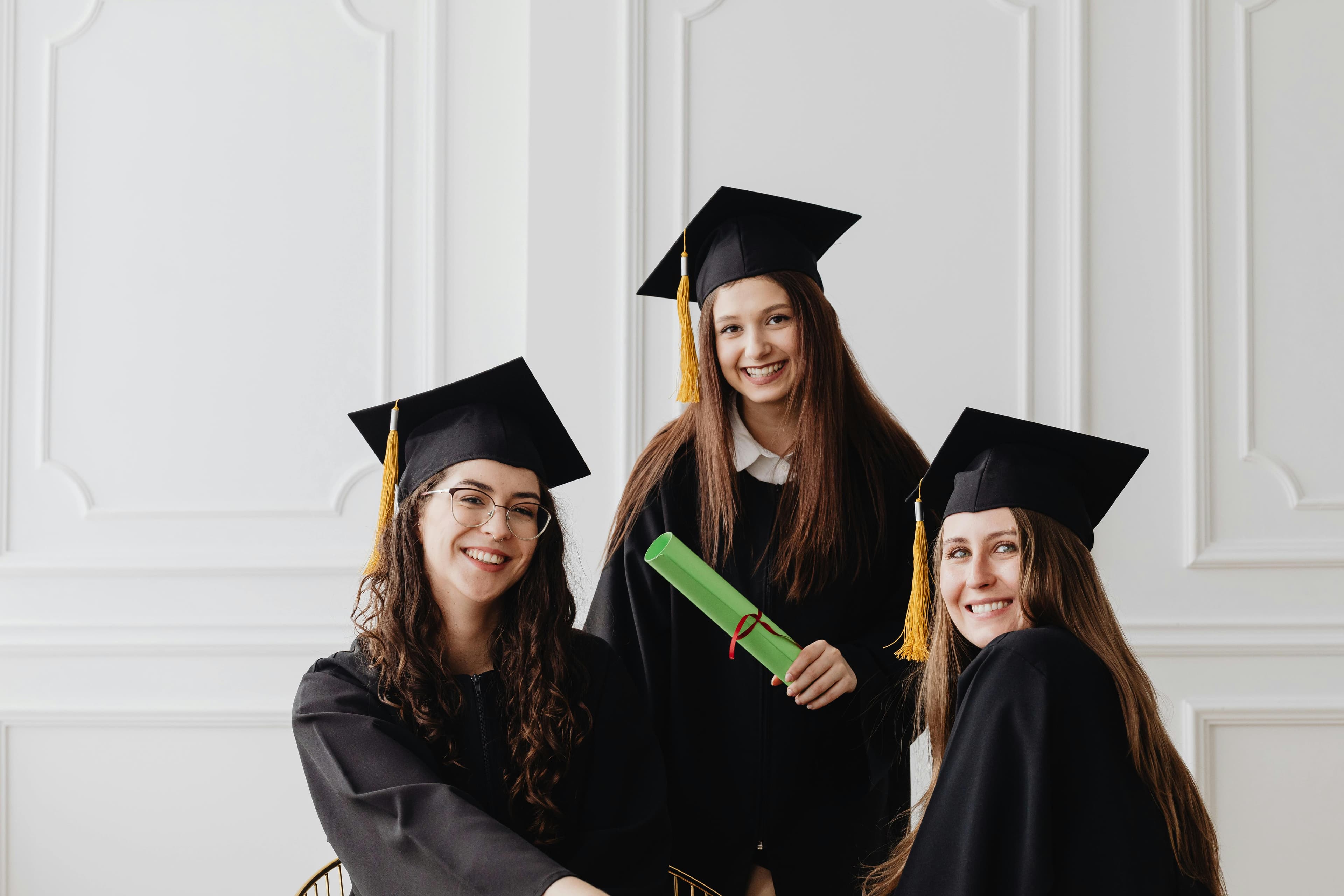 Three young women celebrating graduation with caps and diplomas indoors.