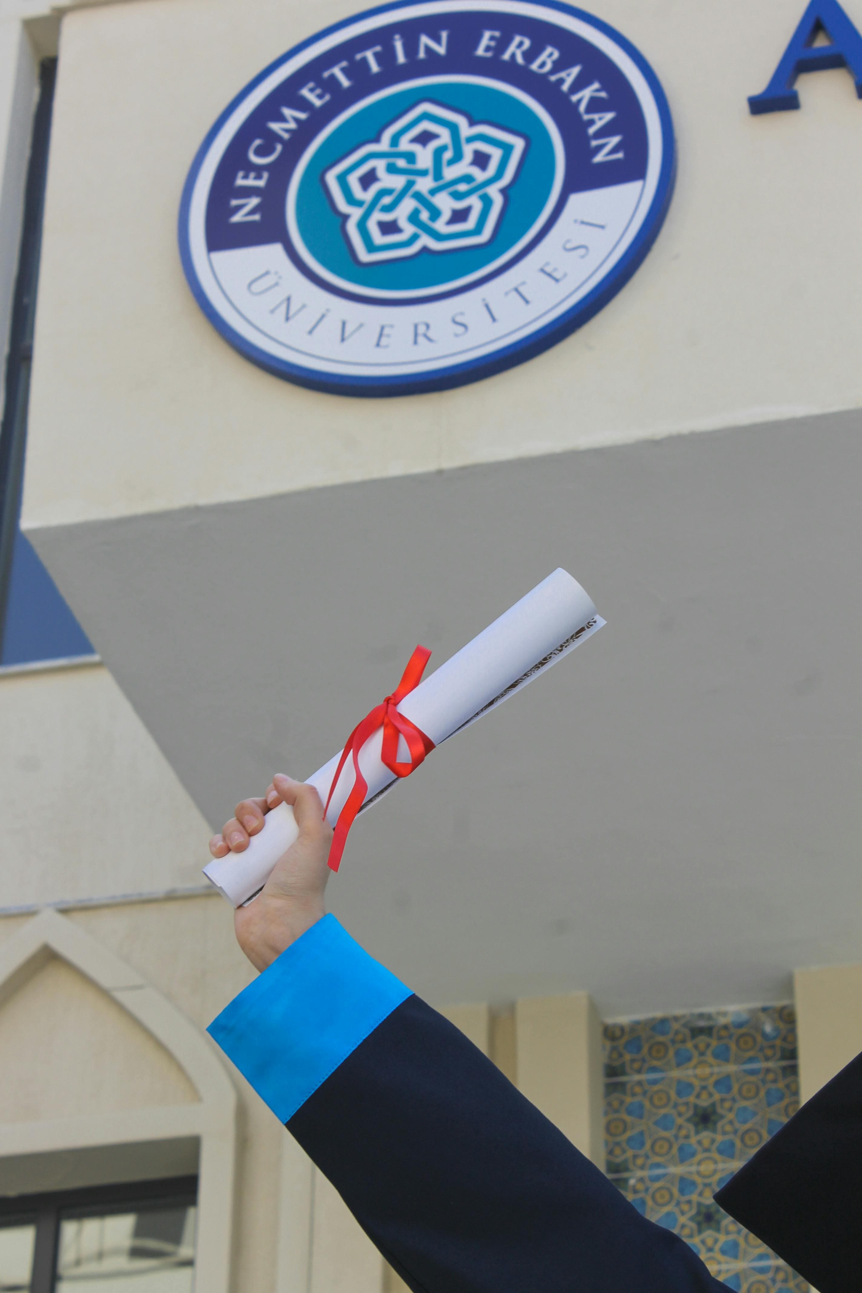 Necmettin Erbakan University 표지판 앞에서 졸업장을 든 졸업생. 성공을 축하합니다.