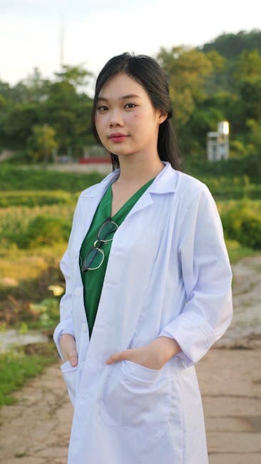 Asian female doctor in a lab coat standing outdoors, conveying a sense of calm confidence.