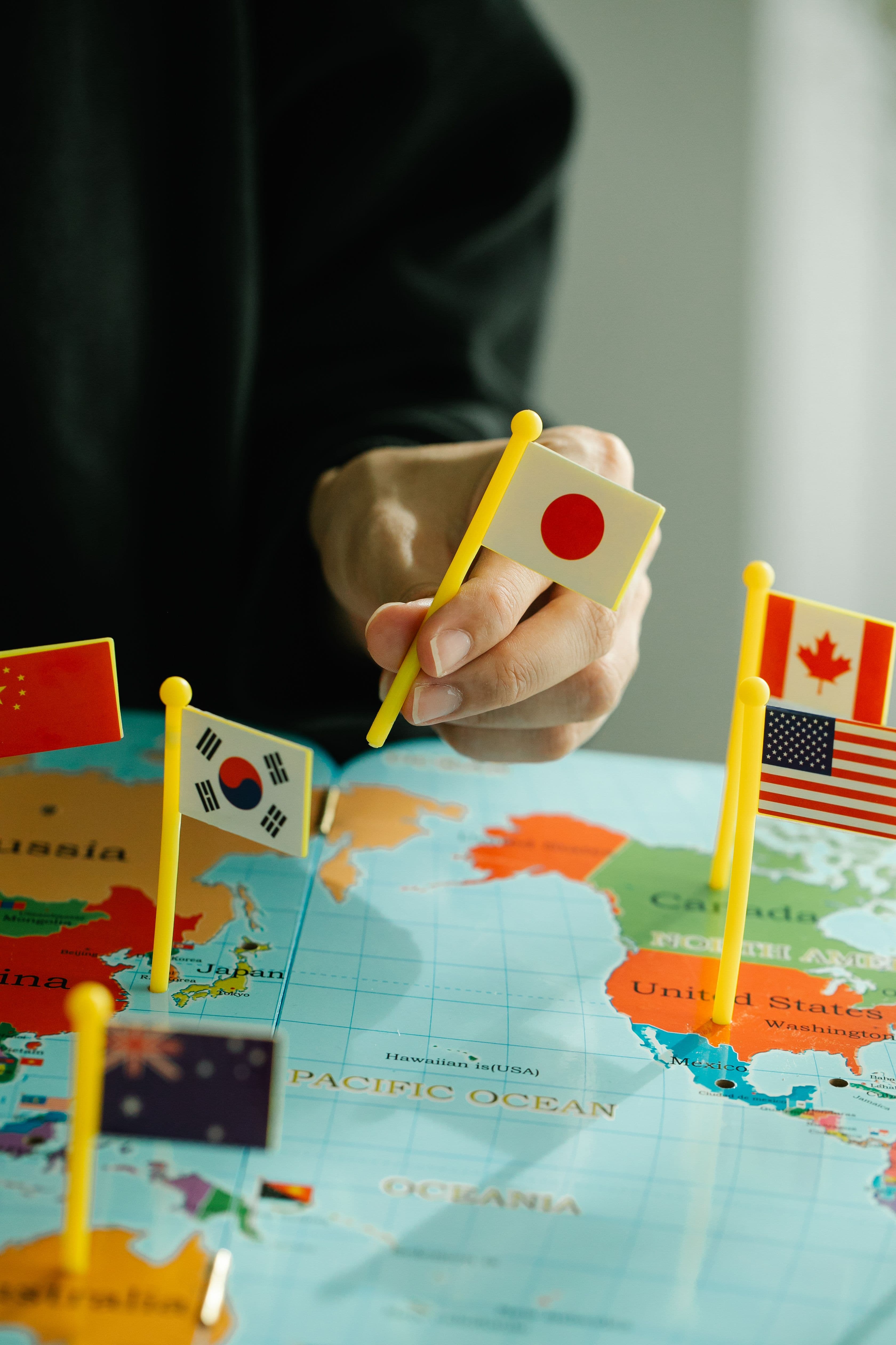 Gros plan d'une main plaçant le drapeau japonais sur un planisphère entouré de divers drapeaux nationaux.