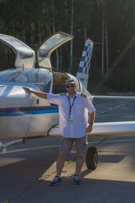 Pilot in uniform stands confidently beside a small aircraft on a sunny day.