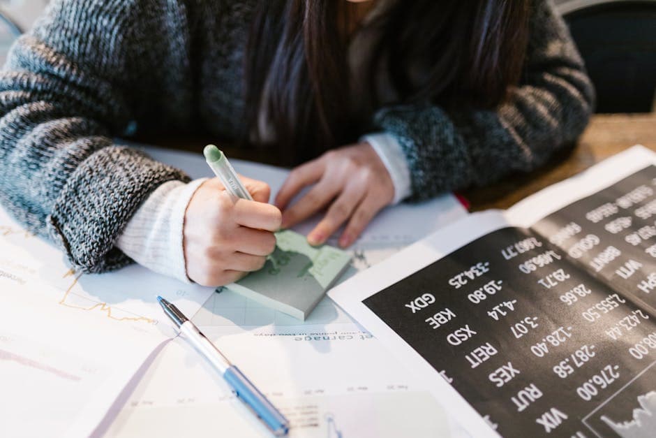 Close-up of a person writing on a sticky note amidst documents in an office setting.
