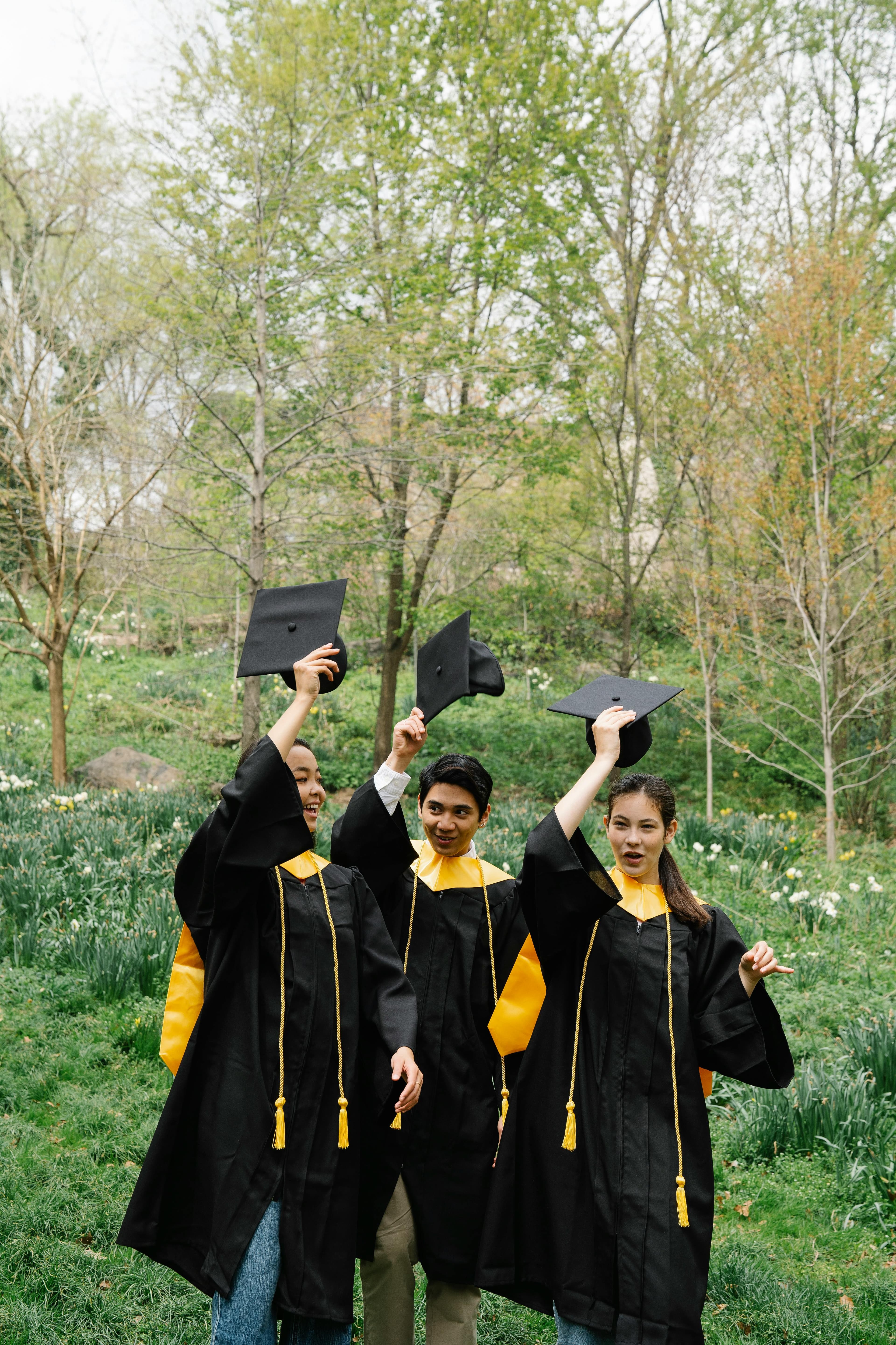 Three young graduates celebrating their success in an outdoor spring setting.