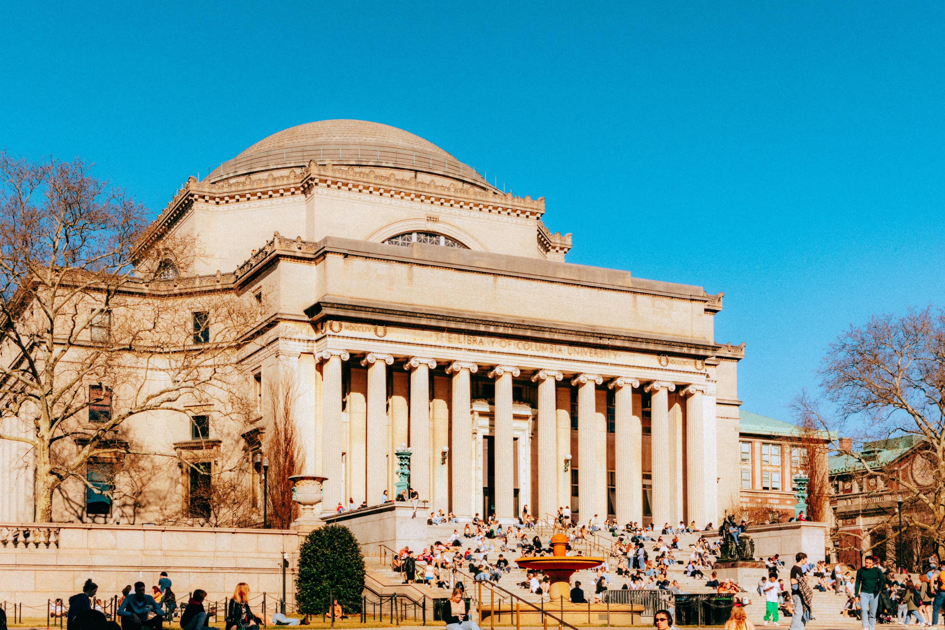 Historic library at Columbia University with people gathered on steps under clear sky.