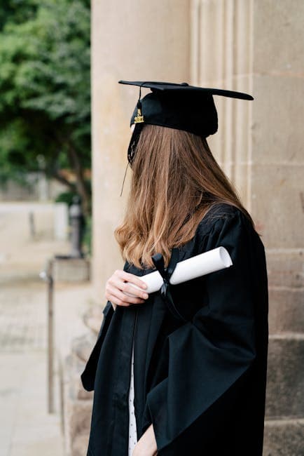 A young woman in a graduation gown holding a diploma standing outdoors.
