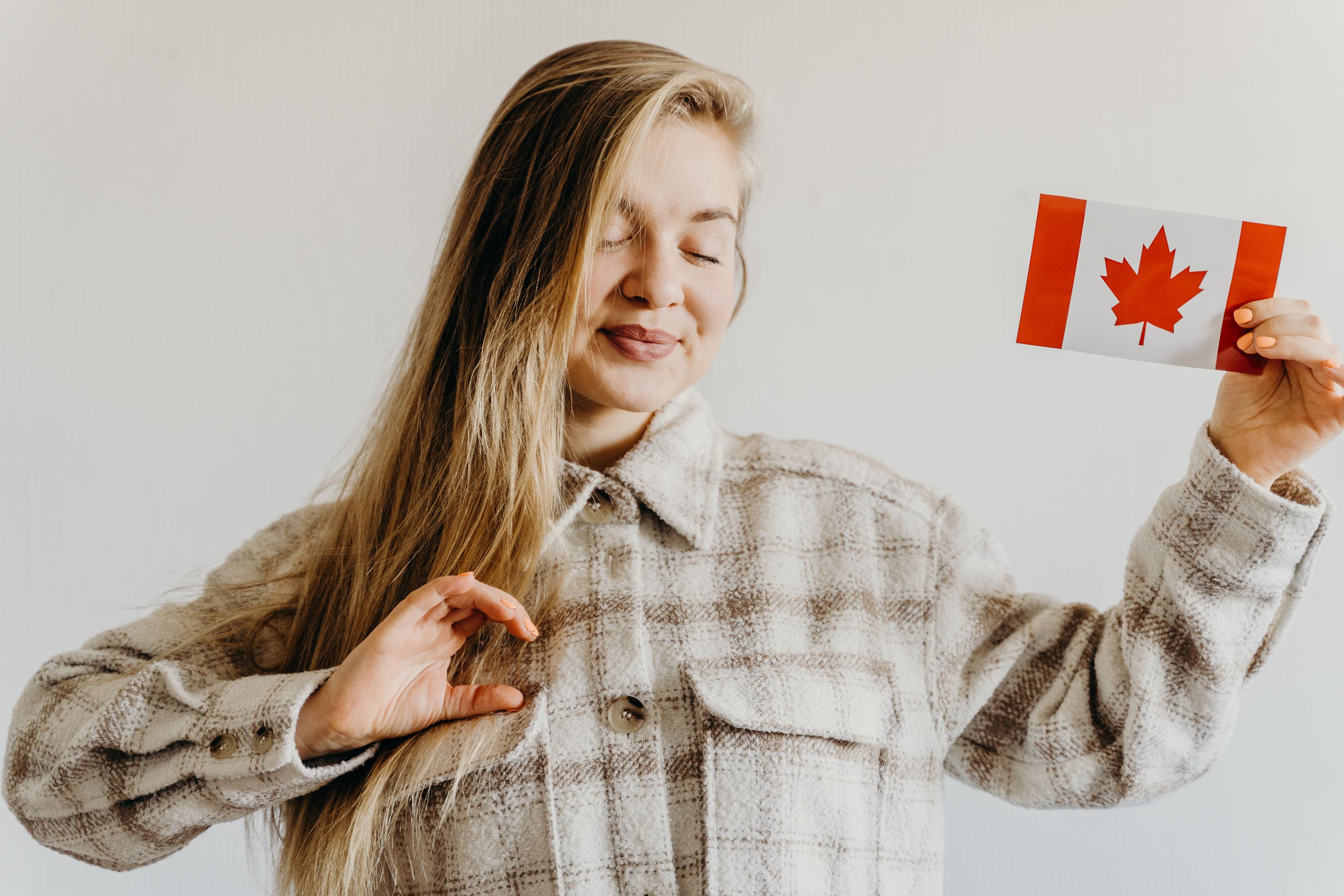 Femme blonde aux yeux fermés tenant un drapeau du Canada, symbole de fierté et de célébration.