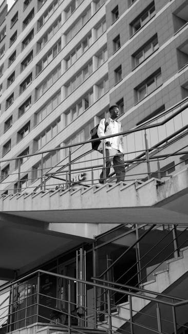 Monochrome photo of a man walking on stairs outside a tall building.