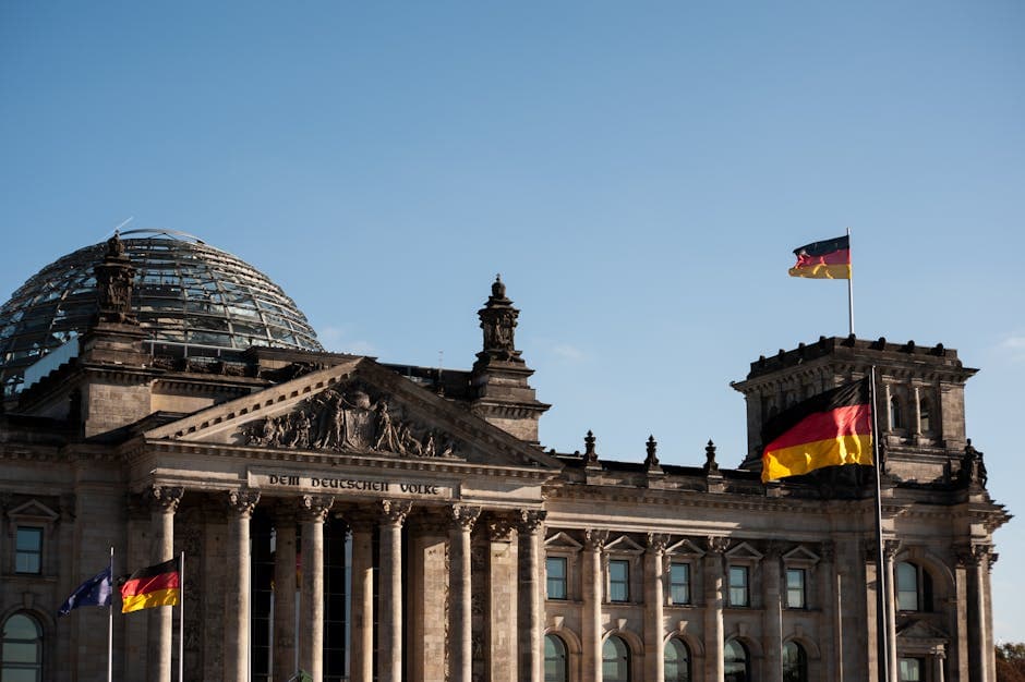 Historic Reichstag building in Berlin with prominent German flags displayed under a clear blue sky.