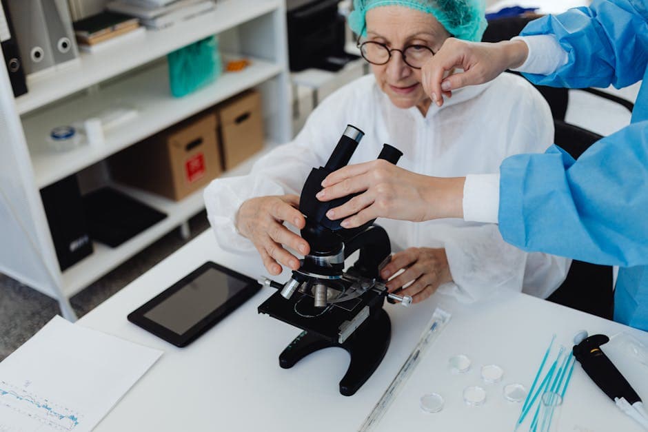 Senior scientist using a microscope with assistance in a laboratory setting, demonstrating research and analysis.