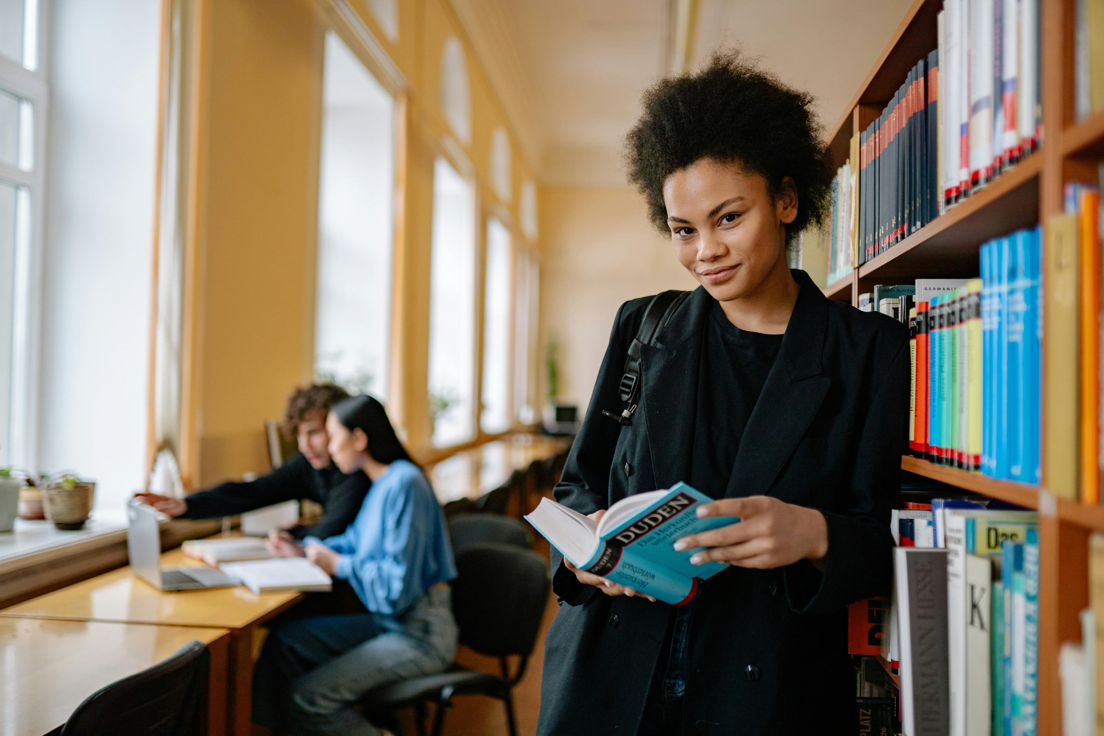 امرأة أمريكية من أصل أفريقي تقرأ كتابًا في مكتبة مضيئة، تجسد المعرفة والتمكين.