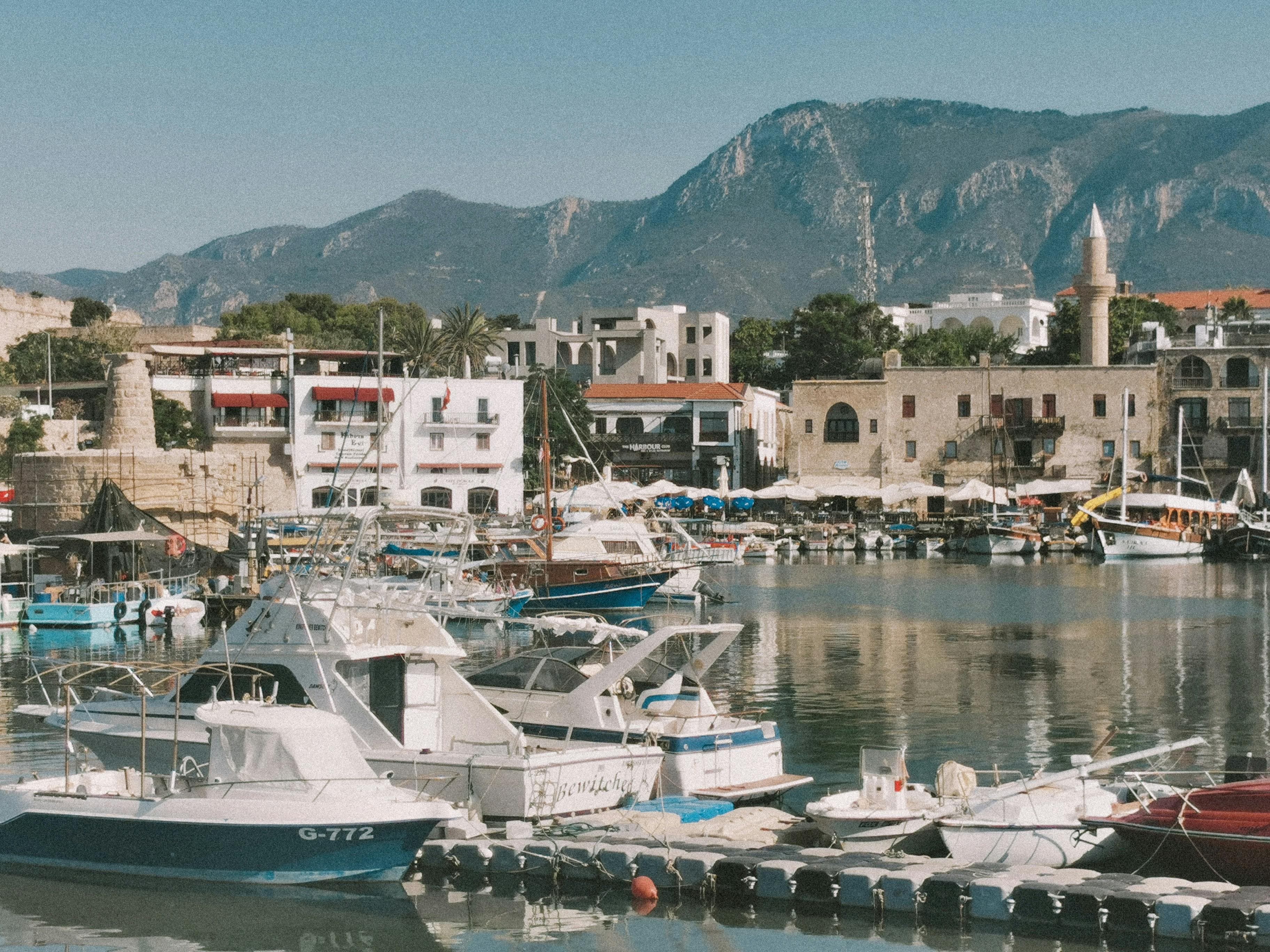Girne Limanı'nın demirlemiş tekneler, tarihi binalar ve arka planda dağlarla güzel manzarası.