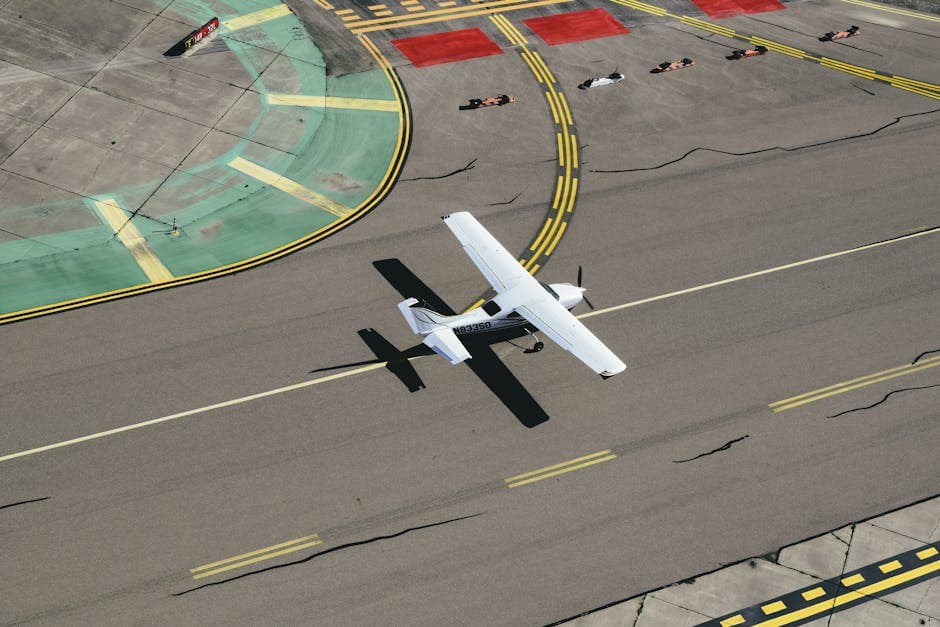 From above of small biplane landing on runway with cracks and yellow markings on summer sunny day