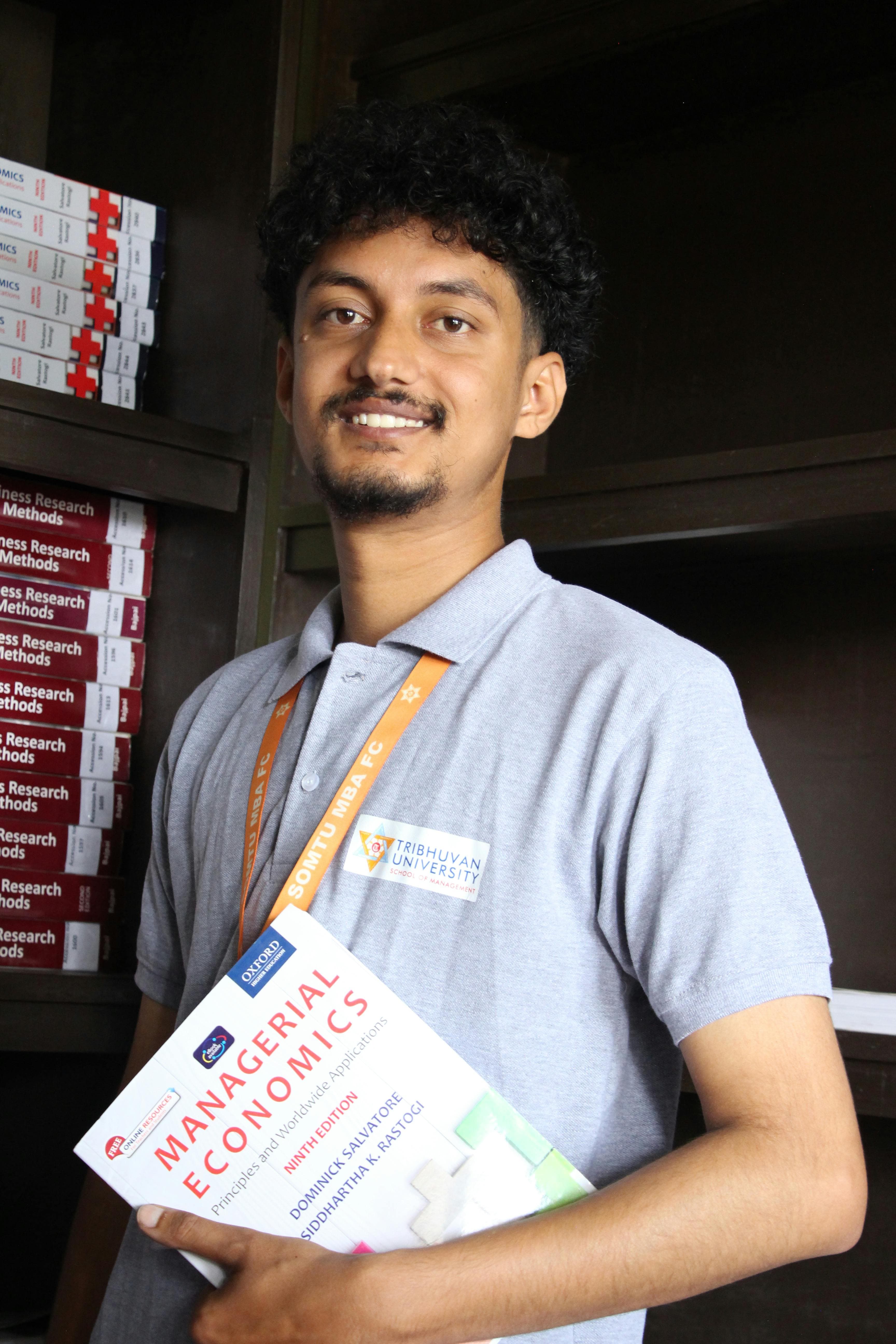 Young student in a university library holding an economics textbook, symbolizing higher education and academic pursuits.